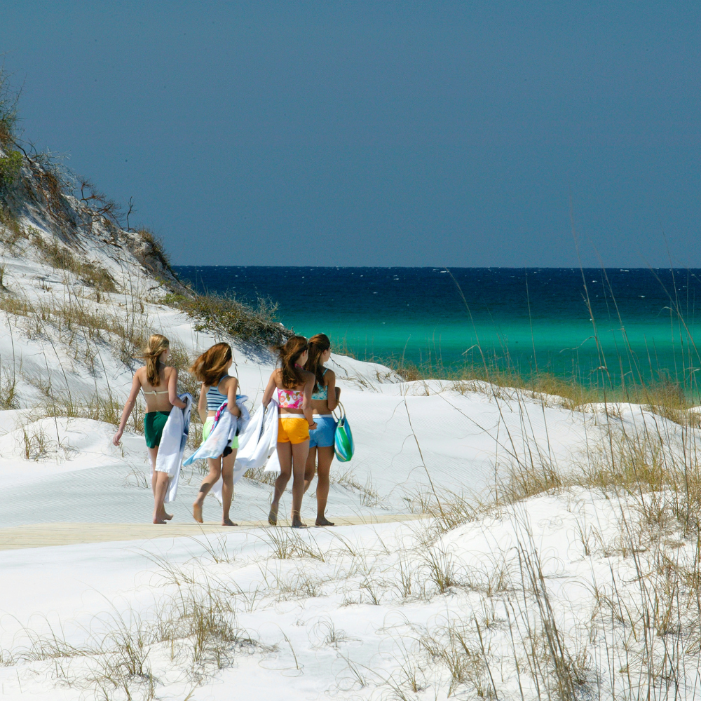 Girls walking to the beach on Florida's 30A, surrounded by white sand dunes and emerald Gulf waters.