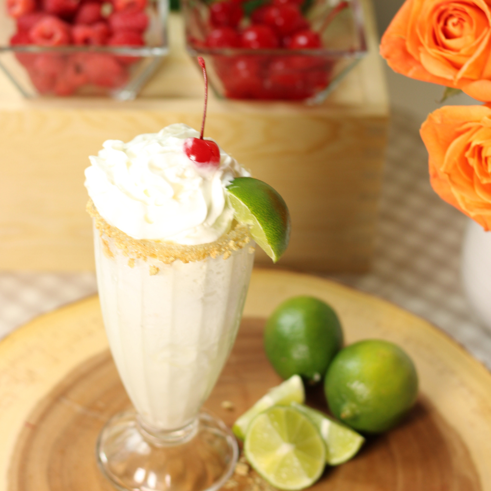 Key lime dirty soda float with lime sorbet, lemon-lime soda, and coconut syrup in a clear glass, topped with a creamy swirl and fresh lime wedge