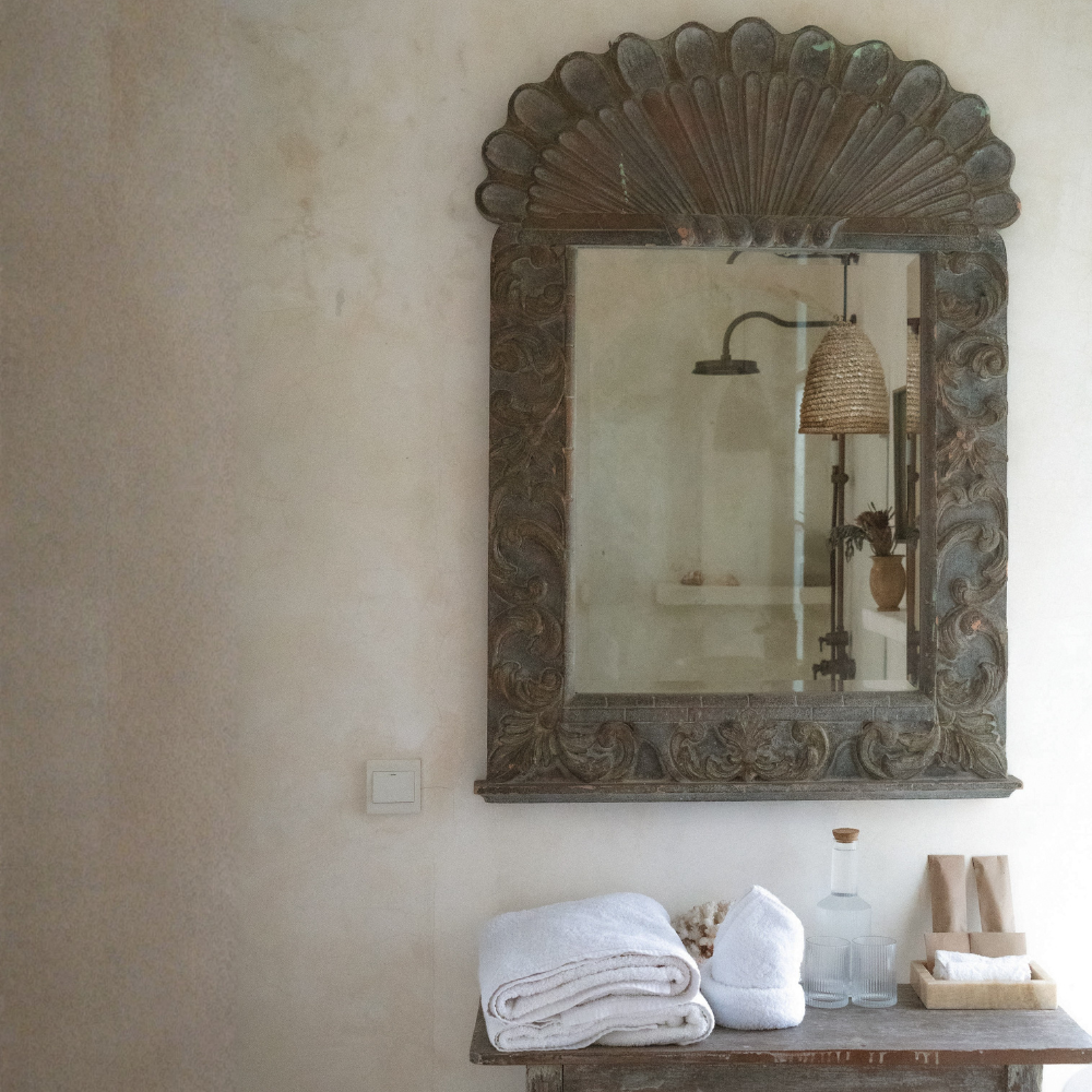 A guest room with plush towels, a water carafe, and guest gifts