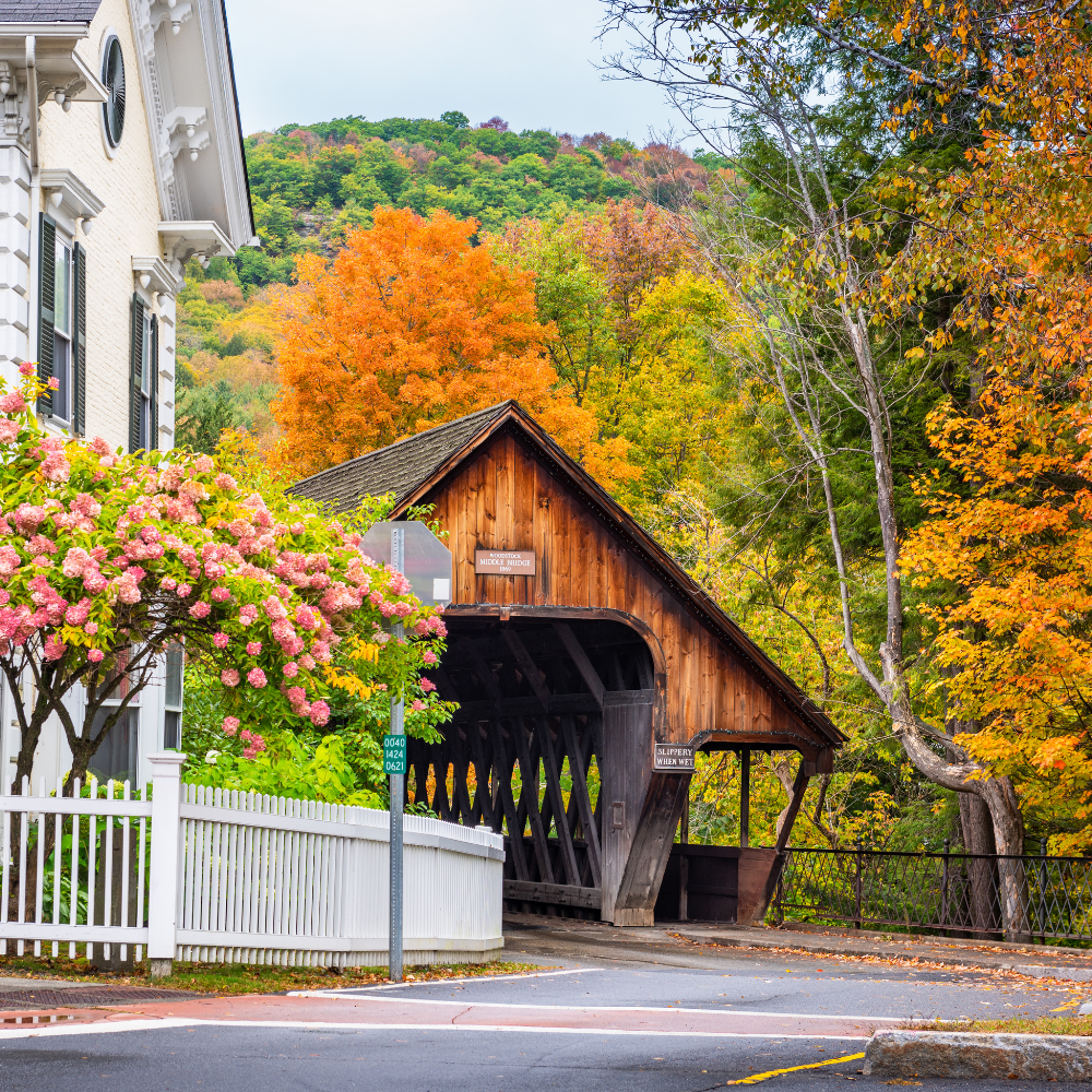 Alt text: Covered bridge in Woodstock, Vermont, surrounded by colorful fall foliage and historic New England homes.